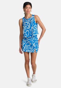 Μπλε αμάνικη μπλούζα με σχέδιο και αντιστοιχισμένο μίνι φούστα, και τα δύο με αφηρημένα λευκά σχέδια. Το σύνολο συνοδεύεται από λευκά αθλητικά παπούτσια.