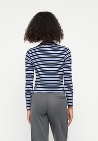 Striped langermet topp i marineblå, hvit og lyseblå, med en tettsittende design og ribbet tekstur. Minimalistisk krage og sømdetaljer på baksiden.