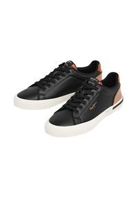 Zapatillas negras de cuero con suela de goma blanca, que presentan un detalle texturizado en tono marrón claro en el talón y cordones negros. Detalle de logo dorado en el lateral.