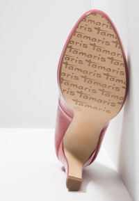 Escarpin rouge à talon aigu, avec un bout pointu, montrant la semelle embossée d'un motif de texte "tamaris" et de la taille 37, positionné sur des surfaces blanches.