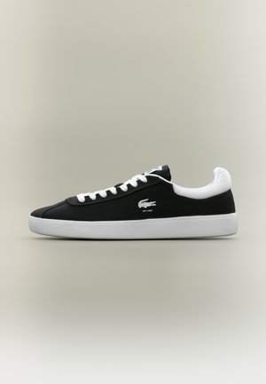 Baskets basses noires et blanches avec des lacets blancs, une semelle blanche et un petit logo crocodile sur le côté.