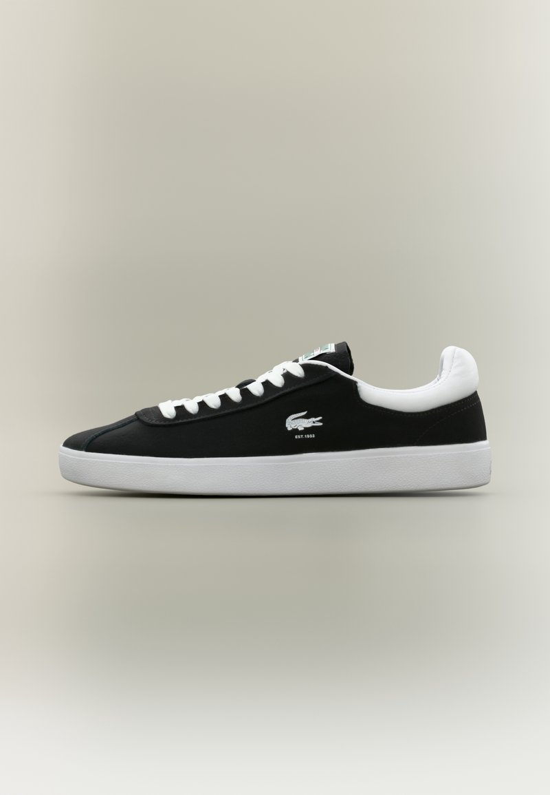 Baskets basses noires et blanches avec des lacets blancs, une semelle blanche et un petit logo crocodile sur le côté.
