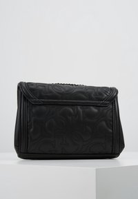 Black leather handbag with embossed logo design, structured shape, and a folding flap. Features a metallic chain accent on the top.