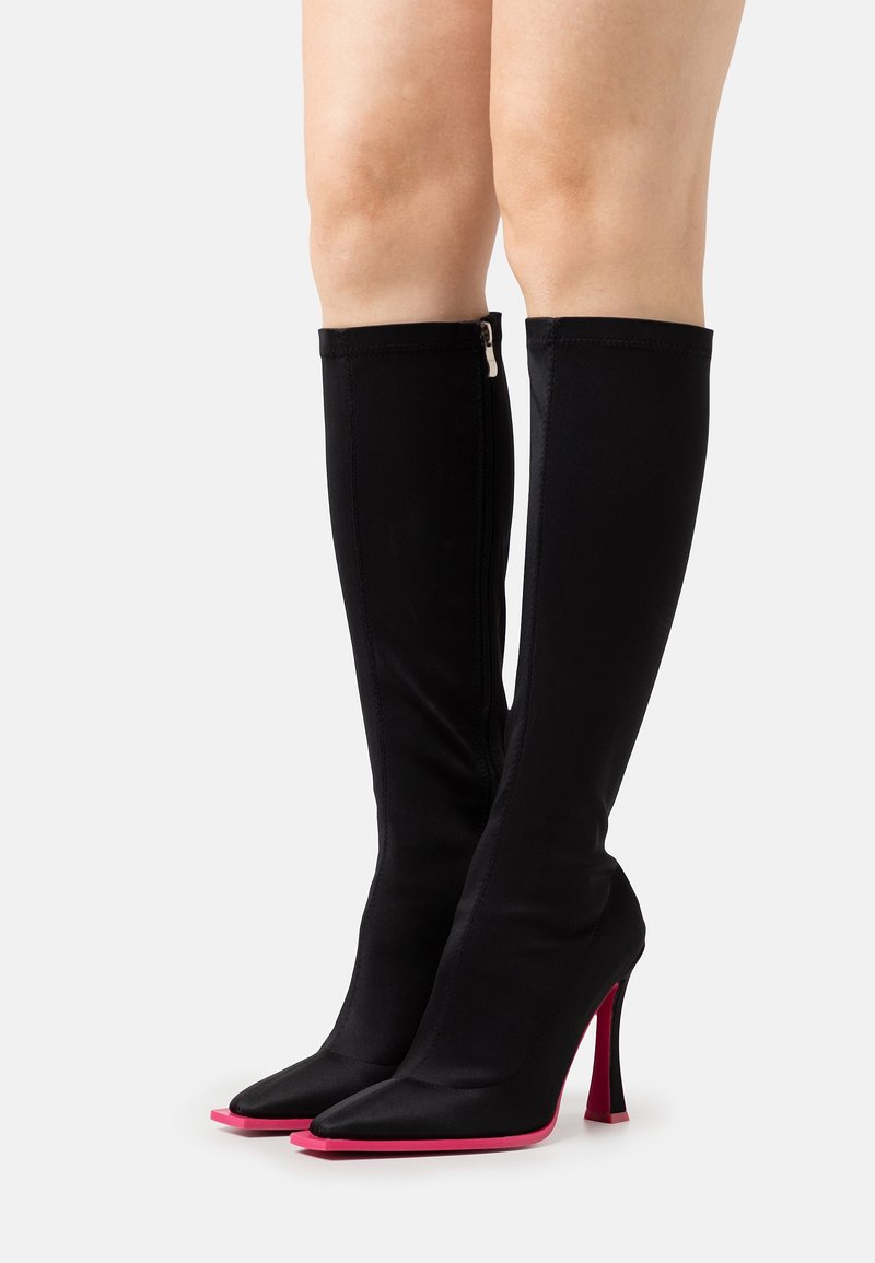 Bottes noires montant jusqu'au genou, en tissu lisse, avec un bout pointu et un accent rose saisissant sur le talon et la semelle. Fermeture éclair à l'arrière.