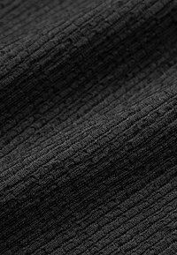 Κοντινή λήψη μαύρου ριμπ ύφανσης με υφή κάθετων γραμμών και απαλά πτυχώσεις που δημιουργούν σκιές και βάθος.