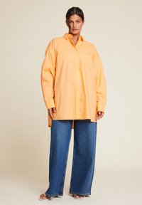 Overdimensjonert oransje skjorte laget av bomull, med lange ermer, krage og en brystlomme, kombinert med vide blå denimjeans.