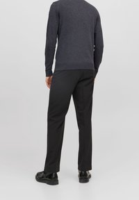 Mörkgrå tröja med texturerad yta, parat med svarta smala byxor och svarta skor, sedd från baksidan mot en neutral bakgrund.