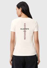 T-shirt en coton crème avec un design graphique vertical au dos, avec "ALLSAINTS" en lettres noires en gras et un petit élément décoratif en rose.