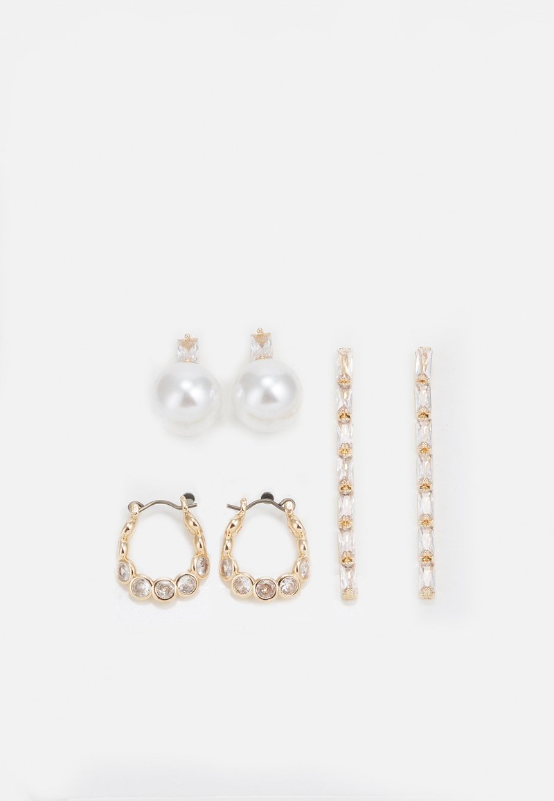 Trois paires de boucles d'oreilles : de grandes perles blanches en boutons, des créoles en or avec des pierres claires, et deux longues boucles d'oreilles droites en or avec des détails scintillants.