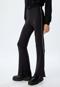 Zwarte flared pants van rekbare stof met witte zijkanten. Heeft een hoge tailleband en een gladde textuur. Gecombineerd met robuuste zwarte laarzen.