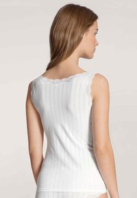 Canottiera bianca con righe verticali, dettaglio in pizzo lungo il colletto e le aperture per le braccia, caratterizzata da un design aderente e realizzata in morbido cotone.
