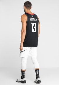 Maillot de basket-ball noir avec des accents rouges, affichant "HARDEN" et le numéro "13" au dos. Shorts blancs et chaussettes noires à motifs.