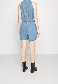 Džínový overal s upnutým korzetem, elastickým pasem a krátkými nohavicemi. Obsahuje límeček a zadní kapsy. Nosí se s černými kotníkovými botami.