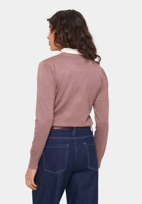 Light mauve pullover sweater with long sleeves and ribbed collar, paired with dark blue jeans. Soft texture, fitted design, and puffed shoulders.