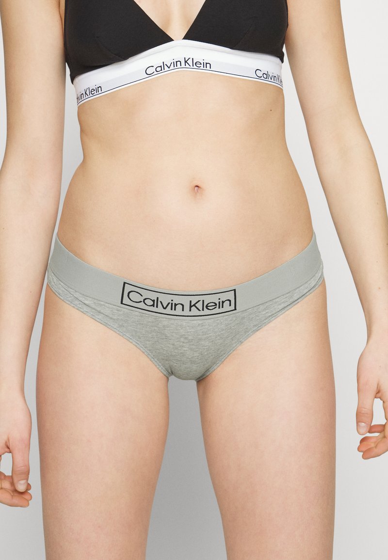 Sive bombažne hlačke z širokim pasom, na katerem je logo Calvin Klein. Oblikovanje je minimalistično z gladko teksturo.