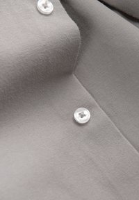 Gros plan sur un tissu gris avec deux boutons en plastique transparent cousus avec du fil gris.