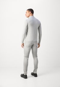 Pull en tricot gris avec un col rabattu, associé à un jean skinny gris clair et des chaussures noires, vu de dos.