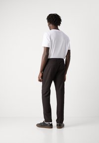 Black trousers with a slim fit, featuring two back pockets and a smooth fabric texture. Paired with a plain white T-shirt and sneakers.
