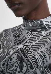 Top de cuello alto en blanco y negro con estampados gráficos, que incluyen texto e ilustraciones, con una textura de tela suave y elástica.