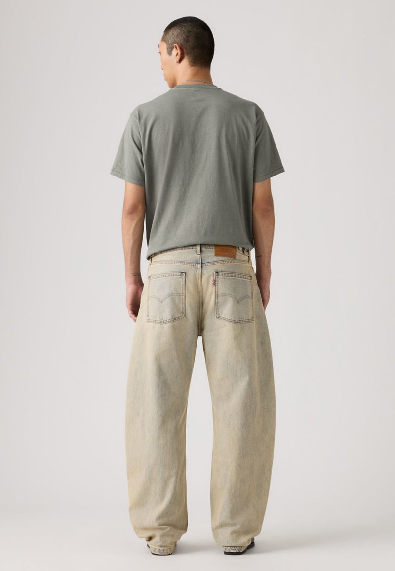 T-shirt grigia in cotone abbinata a jeans azzurri dal taglio ampio. I jeans presentano una lavatura chiara, gambe dritte e tasche posteriori con cuciture visibili.