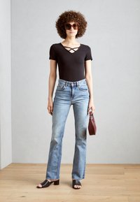 Svart kortermet bodysuit med kryssdesign, lyseblå høy midje jeans, og svarte hælsandaler. Holder en liten burgunderveske.