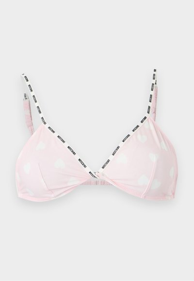 Ανοιχτό ροζ bralette με λευκά σχέδια καρδιών και λεπτές ασπρόμαυρες λωρίδες με λογότυπο, απλωμένο επίπεδα σε γκρίζο φόντο.