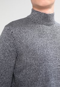 Maglione grigio a collo alto con un motivo tessuto, caratterizzato da un colletto alto e un design aderente. Il tessuto sembra morbido e accogliente.