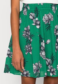 Groene bloemenrok gemaakt van lichte stof. Bevat zwart-witte bloemenpatronen en heeft een elastische tailleband, met een geplooid ontwerp.