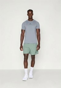 Gray athletic t-shirt with a slim fit and black logo, paired with light green shorts and white athletic shoes, set against a plain background.