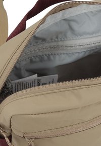 Borsa in tessuto beige con tracolla bordeaux, dotata di apertura con zip, fodera grigia e un'etichetta interna. Include una tasca con zip più piccola.