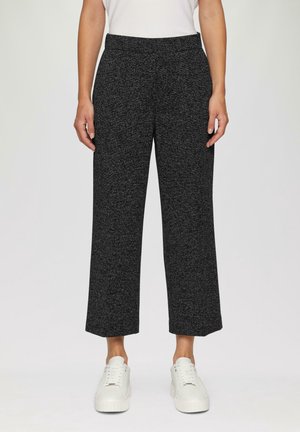 Person wearing wide-leg dark gray knit pants paired with white sneakers and a white top, standing against a neutral background.