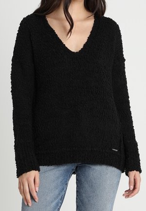 Maglione nero a maglia con texture, scollatura a V profonda e maniche lunghe. Presenta una vestibilità rilassata e un orlo che si estende sotto i fianchi.
