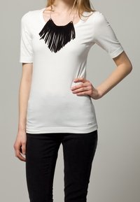 Hvid T-shirt med korte ærmer og et design af en sort frynset halskæde. Skjorten er lavet af blødt stof i fitted stil. Sammen med sorte bukser.