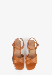 Brown leather sandals featuring crisscross straps, adjustable ankle strap, and a platform sole with a textured edge.