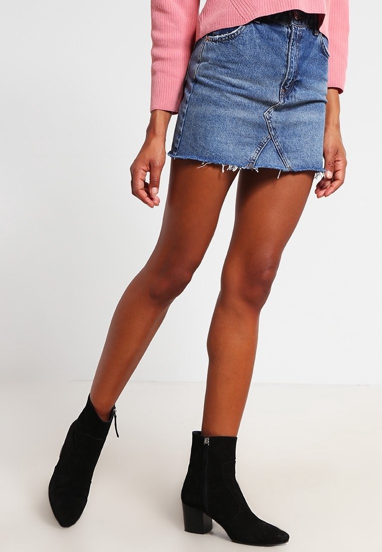 Džínová mini sukně s třepeným lemem, zapínáním na knoflík a zip, a vybledlým modrým odstínem; kombinováno s černými kotníkovými botami.