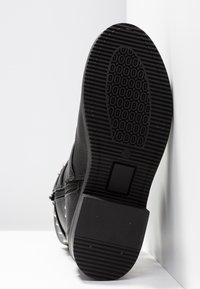 Stivale alla caviglia nero in pelle testurizzata, suola in gomma con motivo antiscivolo, chiusura con cerniera laterale e elementi in metallo sulla parte superiore.