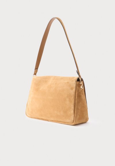 Τσάντα ώμου από καστανό σουέντ με έναν φαρδύ ιμάντα και εξαρτήματα σε χρυσό τόνο σε απλό λευκό φόντο.
