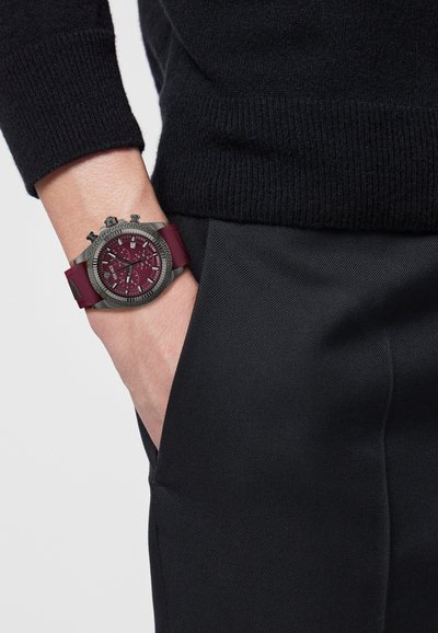 Sportinis laikrodis su bordo spalvos guminės apyrankės dirželiu, tekstūruotu pilku korpusu ir bordo ciferblatu, kuriame yra chronografo funkcijos ir atspindinčios detalės.