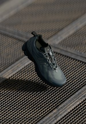 Šedá sportovní bota s texturovaným povrchem, vyvýšeným podpatkem a lehkým designem. Obsahuje šněrování a poutko na zadní straně pro snadné nazouvání.