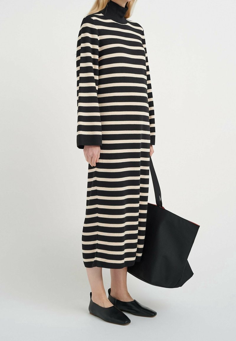 Randig klänning med långa ärmar i svart och kräm, med en hög krage. Matchad med en svart tote-väska och svarta platta skor.