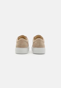 Sneakers in suede beige con design low-top, dotate di una suola in gomma bianca e dettagli cuciti sul tallone. Texture minimalista e liscia.