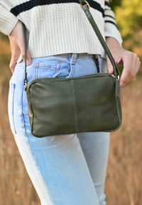 Borsa a tracolla in pelle verde oliva con chiusura con zip e finitura texturizzata, dotata di tracolla rimovibile e design semplice cucito.