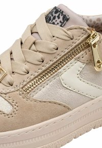 Baskets en suède beige avec un éclat métallique, présentant des détails de fermeture éclair dorés, des accents blancs, une semelle texturée et des lacets beiges entrecroisés.