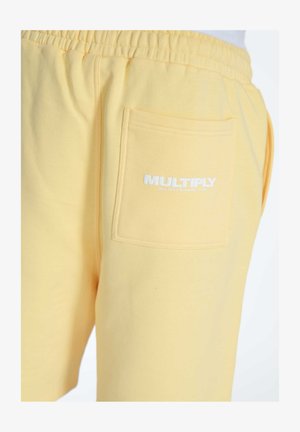 Pantalones cortos de algodón amarillos con una cinturilla elástica, con un bolsillo trasero y un logo blanco de "MULTIPLY". Textura suave y diseño casual.