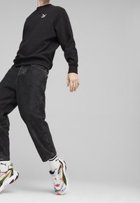 Schwarzes Sweatshirt mit strukturiertem Stoff und gerippten Bündchen, kombiniert mit schwarzen weiten Jeans und mehrfarbigen PUMA-Sneakern. Weiße Socken mit schwarzen Streifen.