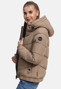Beige gewatteerde jas met een hoge kraag en een afneembare capuchon, voorzien van een zwart logo-embleem op de mouw en een ritssluiting aan de voorkant.