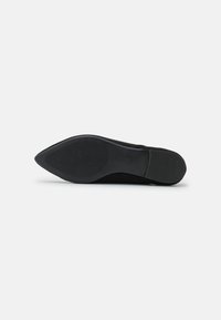 Sorte mockaskinnsåle med spiss tå og teksturert gummigrep. Har et glatt design og flat såle med sirkulære mønsterdetaljer.