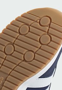 Potplat cipela s teksturiranom gumenu površinom, koji sadrži kružne ispupčenja i rebra, upotpunjen tamnoplavom gornjom stranom i bijelim akcentima.