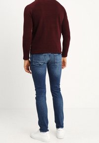 Úzké modré džíny s vybledlým efektem, mají pět kapes a zadní sedlo. Doplněné bordovým tričkem s dlouhým rukávem a bílými teniskami.