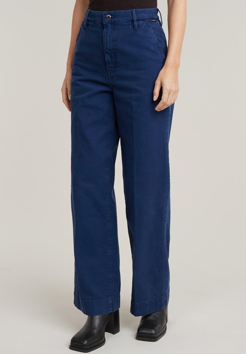 Granatowe spodnie typu wide-leg wykonane z bawełny, z zapięciem na guziki i zamek błyskawiczny, szlufkami na pasek oraz kieszeniami z przodu. Gładka tekstura, proste wykończenie.